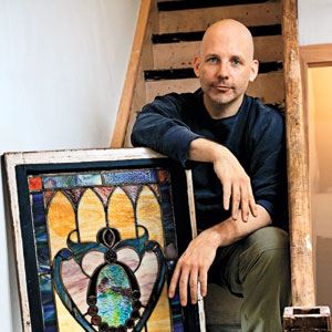 Scott Omelianuk on a stairway leaning on a salvaged stained glass window