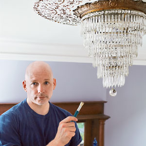 Scott Omelianuk holds up electrical wiring to a chandelier light fixture