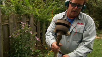 a man wearing safety goggles inspecting the bottom end of a string trimmer