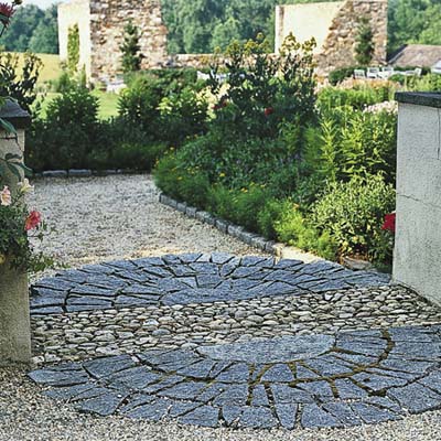 pea gravel underfoot leads to an oval of decorative hardscape of granite semicircles flanked by short stucco pillars