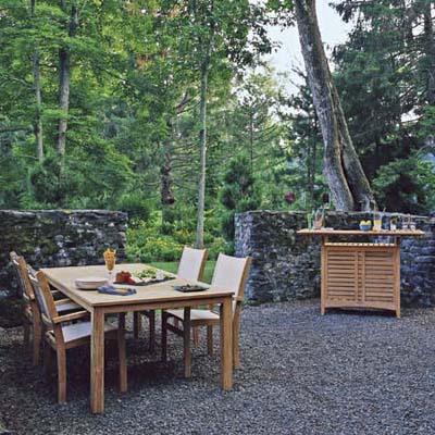 outdoor dining area on gravel bedding, surrounded by woods and rock wall for privacy