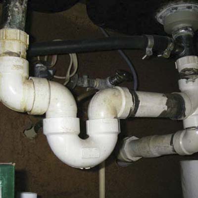underside of a two-bay sink missing a trap on one side and held together by a mystery substance on the other