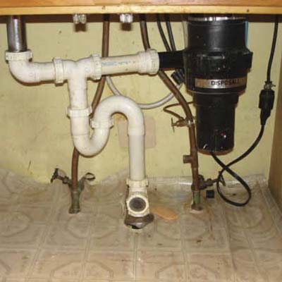 mayhem under a sink including an exposed extension cord, an innapropriate s trap and a clear glass drain line