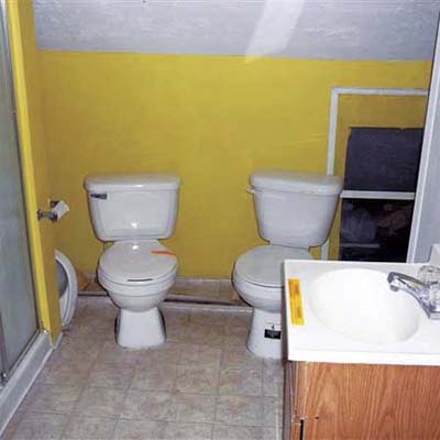 two working toilets installed next to each other in an open bathroom, with no plumbing vent