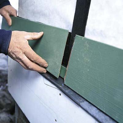 hands replacing damaged clapboard on house exterior