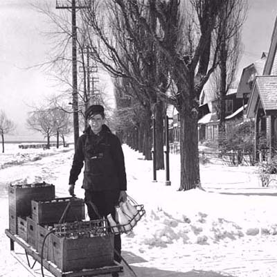 milkman with milk cart making deliveries on a snowy residential street