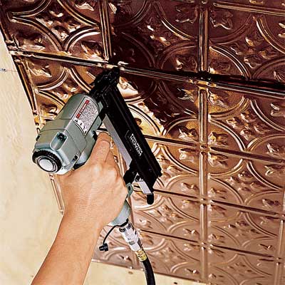 person using a pneumatic nailer to hang tin ceiling tiles