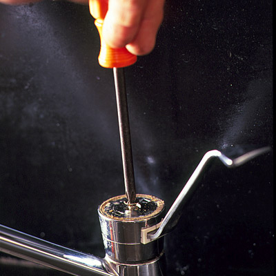 man using screw driver to pop the cap of a faucet
