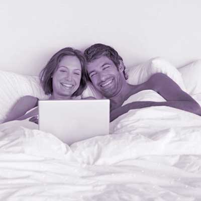 man and woman looking at laptop in bed