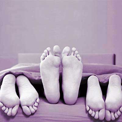 three pairs of feet poking out of sheets at the foot of the bed