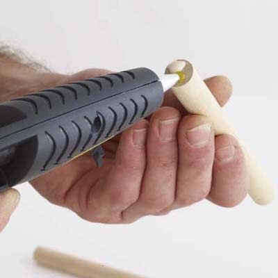 man applying hot-glue to the end of a dowel that already has wood glue on it