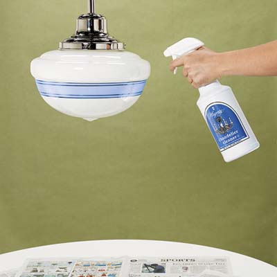 hand holding a spray bottle aimed at the glass shade of a pendant light