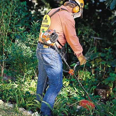 man with safety equipment using string trimmer to cut brush