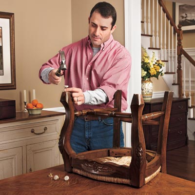 man hammering tacks with felt pads onto bottom of chair leg