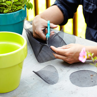 person cutting window screen scraps to fit in flower pots