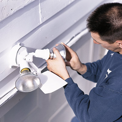man installing sensor on all-night garage floodlight