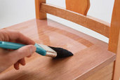 person applies polyurethane to a chair seat with a brush