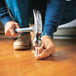 man banging a nail into a floorboard