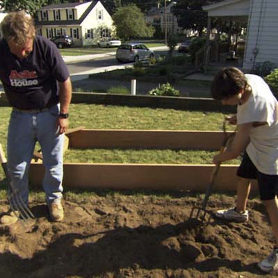 Roger Cook and young boy use pitchforks to turn the soil under the raised garden bed area