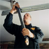 worker installing one of the garage door extension springs to the garage ceiling