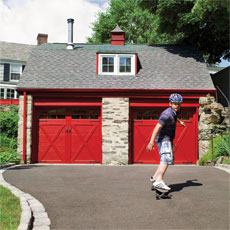 skateboarder rolling downhill from a garage with two red, carriage-style doors