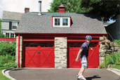 skateboarder rolling downhill from a garage with two red, carriage-style doors