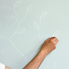 hand shown sketching branches with leaves on a wall with chalk