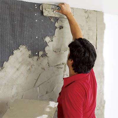 man covering the lath of a fireplace with motar to create a stone veneer surround