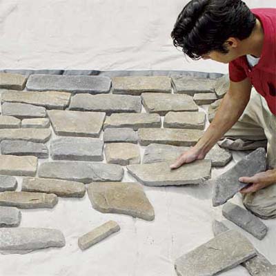 man laying out the stones he'll use to create a stone veneer surround