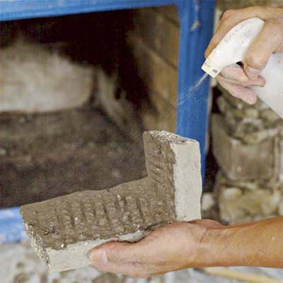 hand with spray bottle wetting down the stone and wall used to create a stone veneer fireplace surround