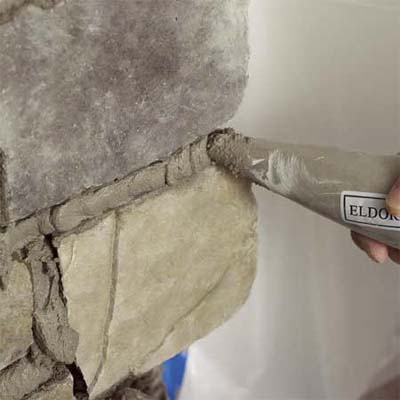 the tip of a grout bag applying grout to the stone when creating a stone veneer fireplace surround