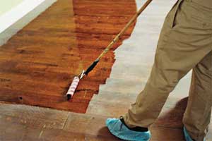 man with booties on his shoes applies a coat of polyurethane finish on a wooden floor
