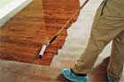 man with booties on his shoes applies a coat of polyurethane finish on a wooden floor