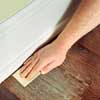 man hand-sanding the perimeter of a wooden floor to prep before refinishing