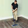 man dry-tacking a freshly buffed wooden floor with a microfiber cloth attached to a flat mop