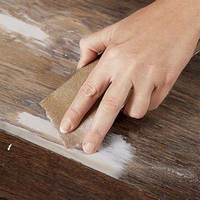hand sanding down dry wood putty on a cabinet door