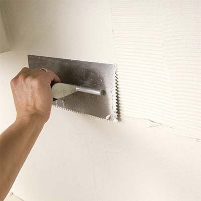 man smoothing the combed thinset while preparing to install a glass mosaic backsplash