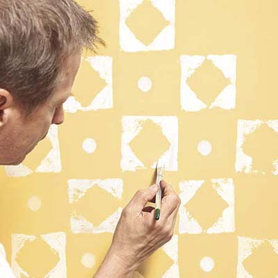man using paint brush to fill in the thin spots after using a stamp to create a decorative pattern