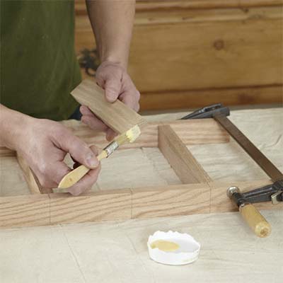 hands brushing glue onto the spindles for building a dog gate