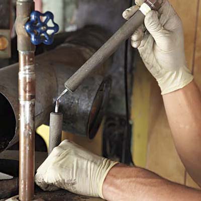 latex-gloved hands check an anode rod from a water heater