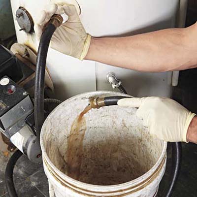 latex-gloved hands hold a hose attached to a water heater that is draining sediment-tinged water
