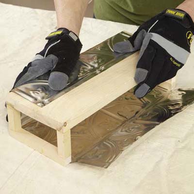 gloved hands wrapping wooden box with tin