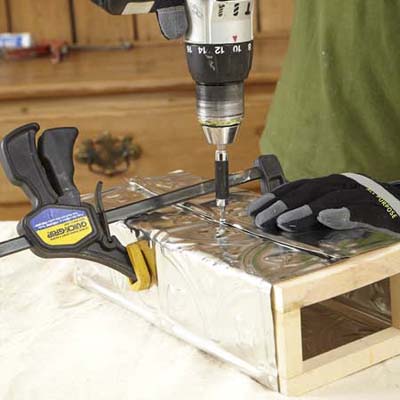 gloved hands nailing tin to wooden box