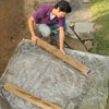 Mark Powers covers his pebble mosaic with a plastic tarp weighed down by 2 4x4s in order to cure the finished mosaic