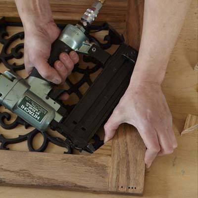Mark Powers uses a pneumatic brad nailer to attach corner blocks to the door frame of a dog crate