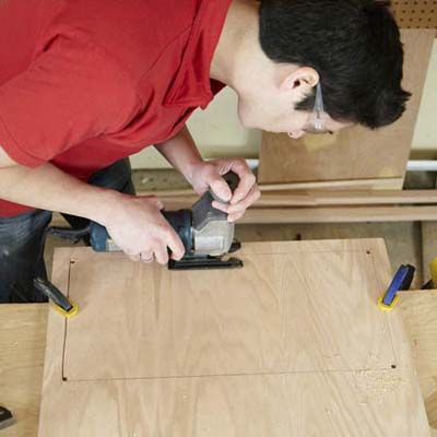 Mark Powers uses a jigsaw to cut out the back window of a dog crate