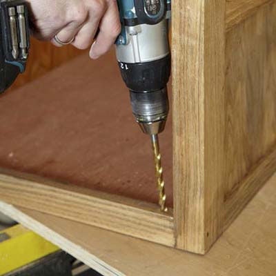 Mark Powers drills a hole for one of the pivot hinges inside the face frame of a dog crate