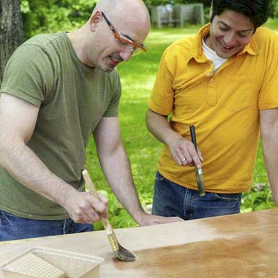two people applying a clear coat of polyurethane to one side of a door