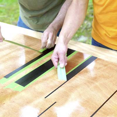 people removing the tape used to mask the lines while building a ricochet game board