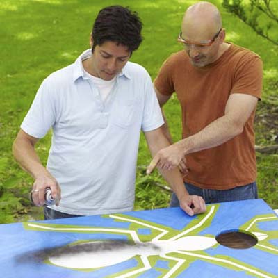 two men painting design for cornhole game board